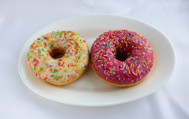 Donuts with strawberry frosting and colorful sprinkles, isolated on a white background on a white plate. Traditional sweet pastries