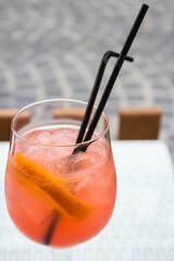 Orange cocktail with ice and two straws.  Aperol spritz cocktail on table. Drinks in outdoor bar. Summer party background. Cool alcoholic cocktails. Refreshing aperitif. Sweet cocktail in street cafe.