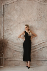 Full-length fashion portrait of a model girl with perfect slim body wearing a black evening dress posing in a minimalist interior