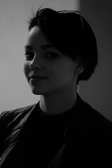 A happy young girl in a black leather jacket and short hair is sitting at a table. Black and white portrait of a smiling woman	