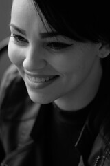 A happy young girl in a black leather jacket and short hair is sitting at a table. Black and white portrait of a smiling woman	