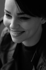 A happy young girl in a black leather jacket and short hair is sitting at a table. Black and white portrait of a smiling woman	