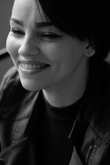 A happy young girl in a black leather jacket and short hair is sitting at a table. Black and white portrait of a smiling woman	