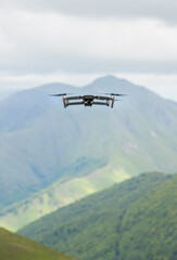 Fototapeta na wymiar Drone flying over mountainous landscape. The drone can be seen from the front and the camera has an ND filter. In the background you can see a mountain and at the bottom a forest and a green meadow.