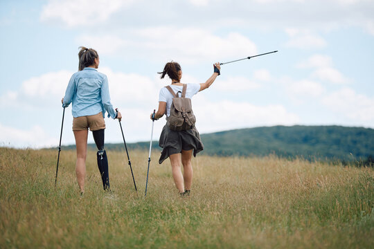 Back view of woman with leg disability and her female friend enjoy in hiking in nature.