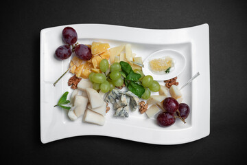 top view of cheese plate with grape, walnuts and honey on black background