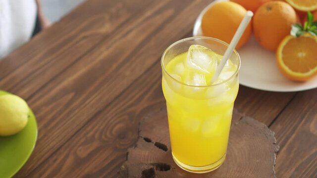 Homemade lemonade. Fresh lemons and oranges on plates. Cold refreshing summer drink with ice in tall glass. Iced summer non-alcoholic drink on wooden kitchen table. Нands insert cocktail tube and mint