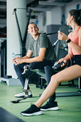 Fototapeta na wymiar Happy sportsman with prosthetic leg and his female friend talking while taking a break from exercising at gym.