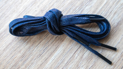 A subject shot of dark blue flat laces with thin tips for shoes rolled up and isolated on a wooden...