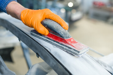 Preparation for painting a car bumper. Hand in a glove with a grinding tool