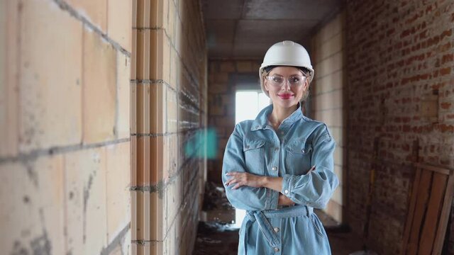 A female architect or bricklayer stands in a newly built house with untreated walls. The process of building housing for the family. Building materials
