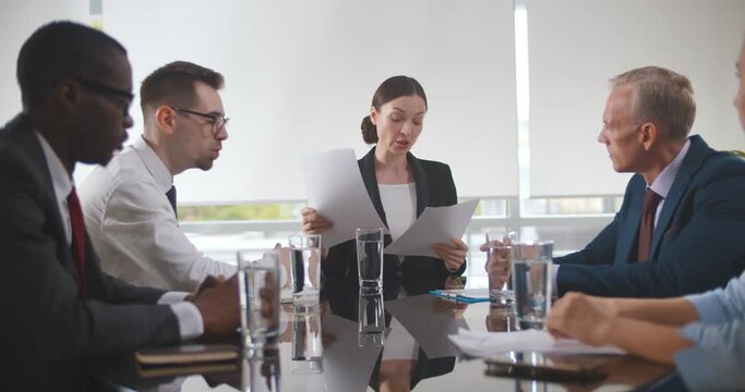 Group of businesspeople sitting in meeting room and listening to female speaker.