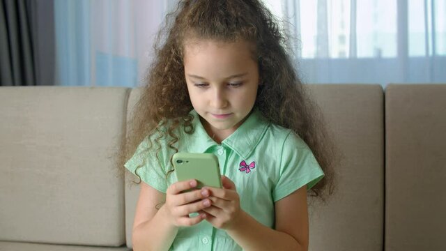 Honey kid using smartphone, child browsing the Internet, talking on smart phone, uses video communication at home on the phone. Portrait cute child girl Schoolboy holds a phone.