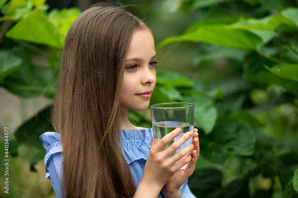 Wall mural cute girl drinking water on the nature background. little young lady holds glass of clean mineral wa