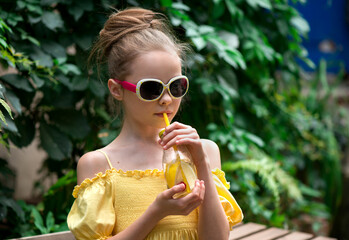 Cute little girl with sunglasses drinks lemonade. Kid holds glass with summer beverage cold tea