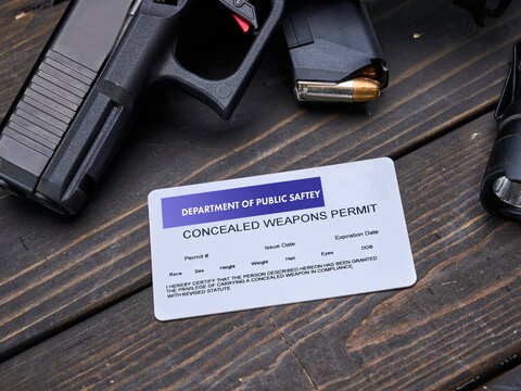 Concealed Carry Permit sitting on a table next to semi-automatic handgun pistol with spare magazine clip