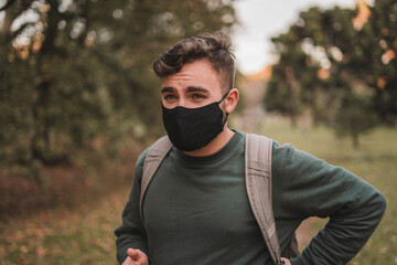 Portrait of a young handsome Caucasian man with mask in a park