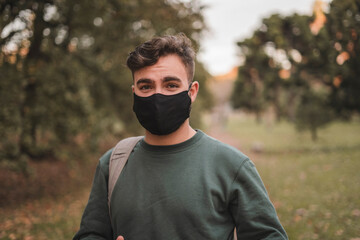 Portrait of a young handsome Caucasian man with mask in a park