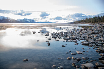 Stunning Canadian lake view in spring summer taken in British Columbia, Atlin with cloudy, blue sky and perfect calm reflection water snow capped mountains scenery. 