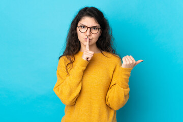 Teenager Russian girl isolated on blue background pointing to the side and doing silence gesture