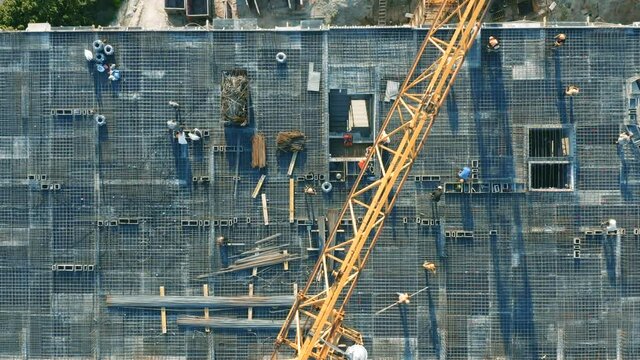 Aerial top down view on the rooftop of an apartment building under construction with tower crane and a lot of workers laying metal rebar