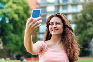 young latin girl with white skin and red hair taking a picture of herself in a park.