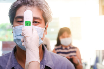 A beautiful Asian female employee wearing a mask and wearing gloves Measure the temperature on the forehead of customers who come to use the service. to prevent coronavirus