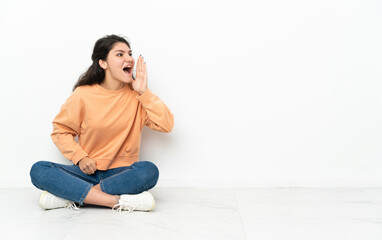 Teenager Russian girl sitting on the floor shouting with mouth wide open to the side
