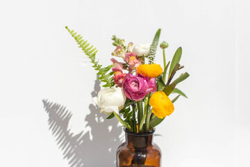 Summer ranunculus floral bouquet in amber vase on white marble backdrop