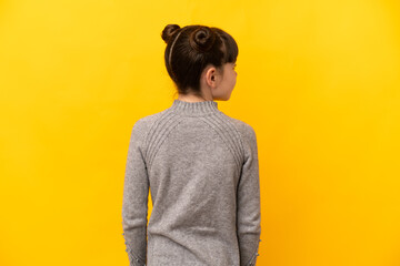 Little caucasian girl isolated on yellow background in back position and looking side