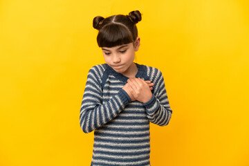 Little caucasian girl isolated on yellow background having a pain in the heart