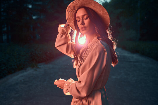 Sexy brunette girl stands with her eyes closed on the road near the forest, the sunset sun shines brightly. Vintage shooting. High quality photo