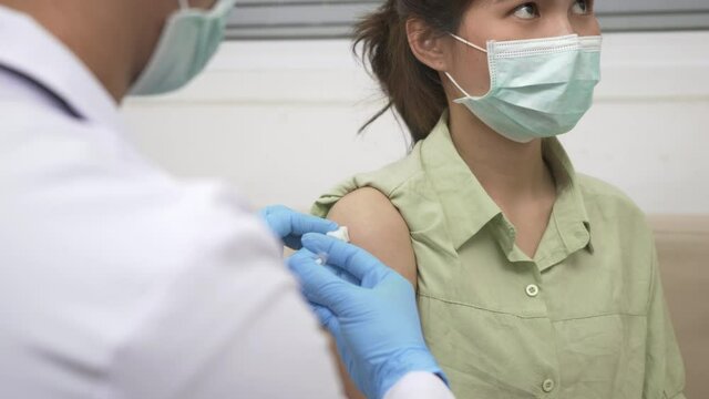 Vaccination, Doctor man after injection coronavirus vaccine to young woman shoulder he rubber protective gloves putting an adhesive bandage plaster, Covid-19 Medicine And Health Care Concept