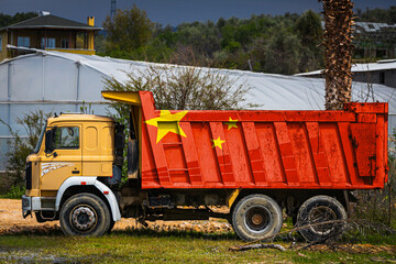 Dump truck with the image of the national flag of China is parked against the background of the countryside. The concept of export-import, transportation, national delivery of goods © Виталий Сова