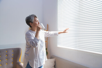 Senior woman drinking coffee next to the window.