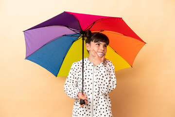 Little girl holding an umbrella isolated on beige background having doubts