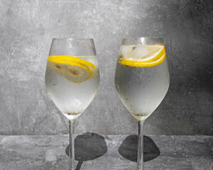 Water with lemon in glasses on a gray concrete background.