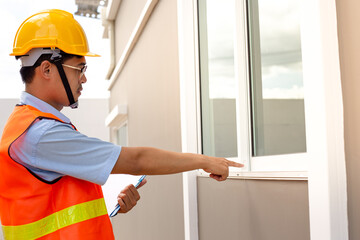 Asian inspector wearing a helmet and safety suit is taking notes after inspecting the structure and exterior of the house building.