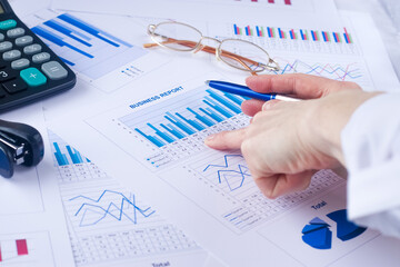 business graph, sales report, calculator, eyeglasses, pen in a hand