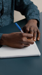 Close up of african american black person taking notes on notepad using a pen. Male adult hands of remote worker writing text on white paper