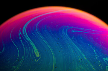 Abstract of a soap bubble. A mix of blue, green, pink and magenta with black background.