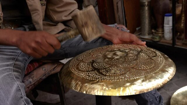 A worker is hammering on a traditional brass lamp to make it smooth. Handicraft work in the Medina of Marrakech, Morocco.