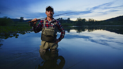 Fly fisherman stands on the river and looks into the camera