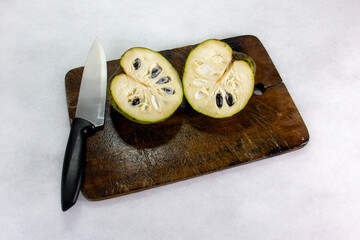 Cherimoya, delicious and exotic Peruvian fruit, cut in two on a wooden board and accompanied by a kitchen knife.