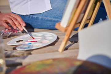 Close-up of female artist taking paint with paintbrush and painting outdoors. Open air. Watercolor painting concepts