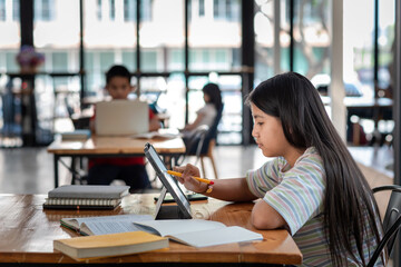 Side view of a girl holding a pen pointing at the tablet screen The book is placed on the table the sides are blurred.