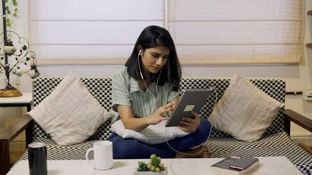 Asian woman using digital tablet while sitting on couch at home. Indian businesswoman use tablet scrolling and touching on screen indoor.social distance. work from home concept. lifestyle concept.
