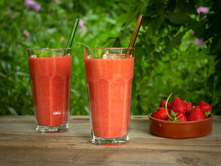 Strawberry smoothie in tall glasses with glass tubes and mint leaves on a wooden table in the garden