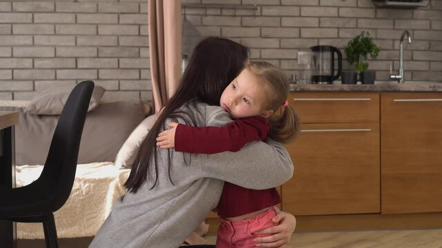A Sad Daughter Hugging Mother at home. Back View of the Brunette Mom with Her Kid, Little Girl with Frustrated Face Embracing Young Woman Indoors