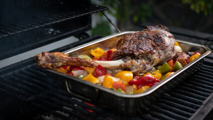 Cooking a delicious leg of lamb on a BBQ with peppers and potatoes in metal tray
